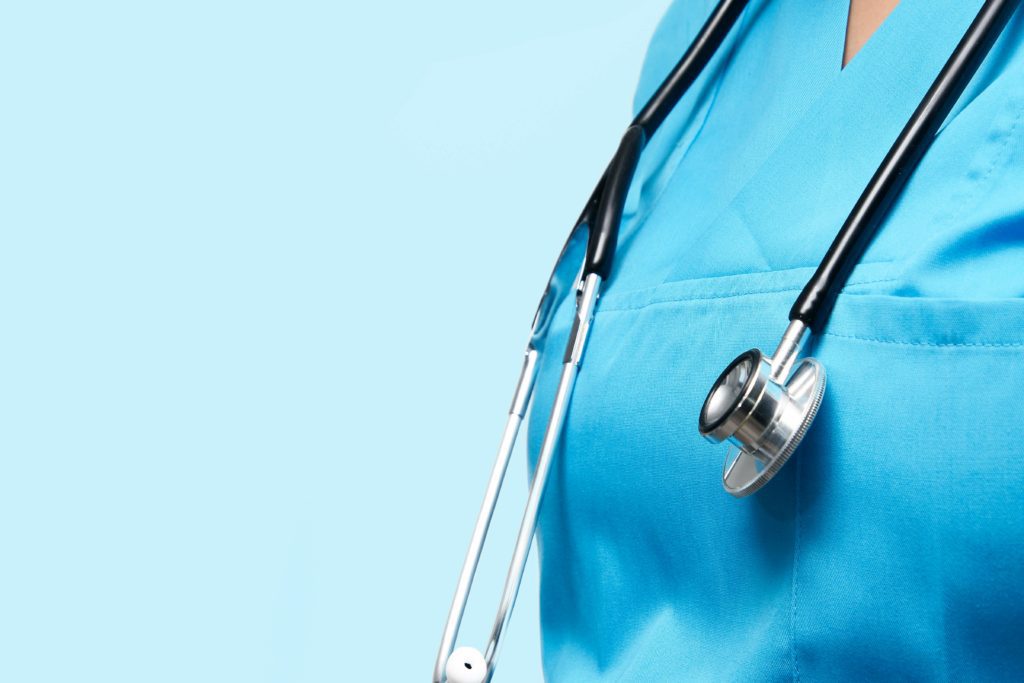 Close-up of a healthcare worker in scrubs with a stethoscope against a blue backdrop.