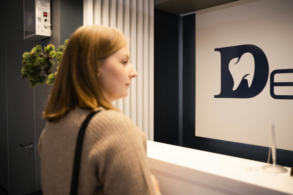 Young woman stands at a dental office reception, side view, casual attire.
