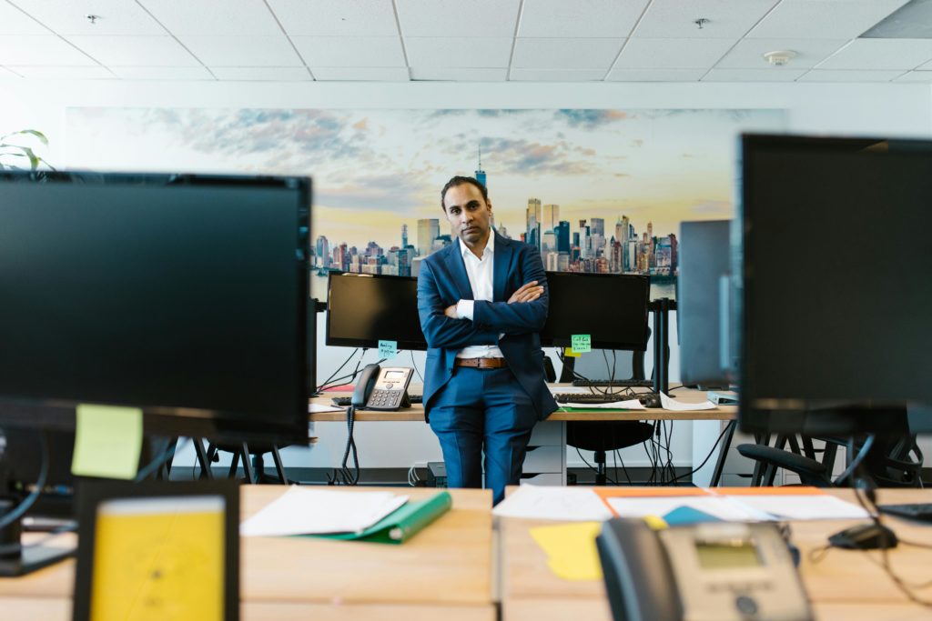 Businessman in a suit stands confidently in a modern office setting with crossed arms.