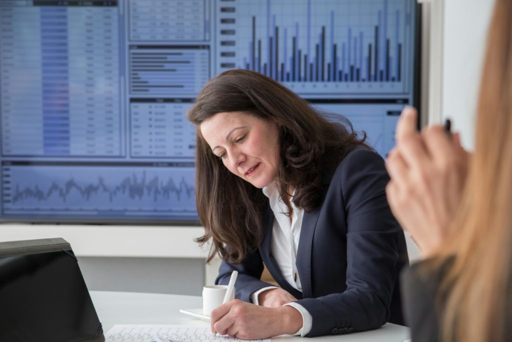 A focused businesswoman analyzing data in an office environment with a statistics screen.